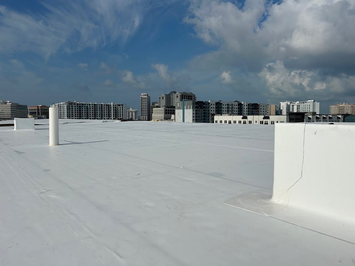 View of a flat white rooftop with vents and city buildings in the background under a partly cloudy sky—expertly maintained by a trusted General Contractor Sarasota FL.