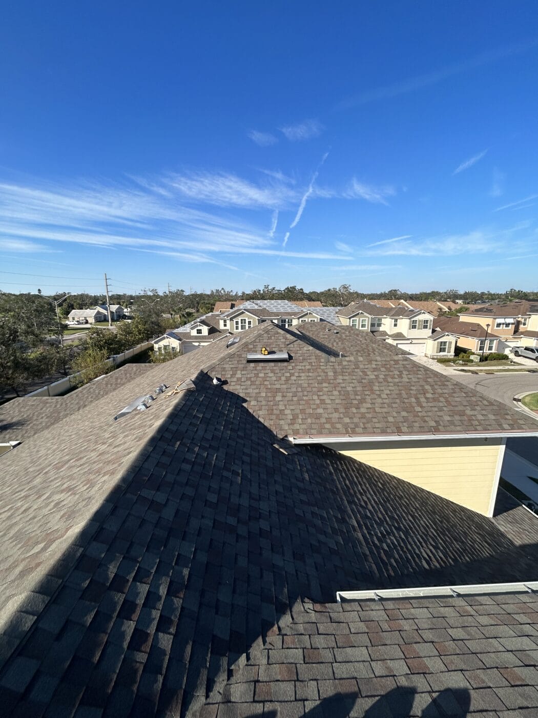 View from a rooftop showing multiple residential homes, clear blue sky, and contrails overhead on a sunny day.