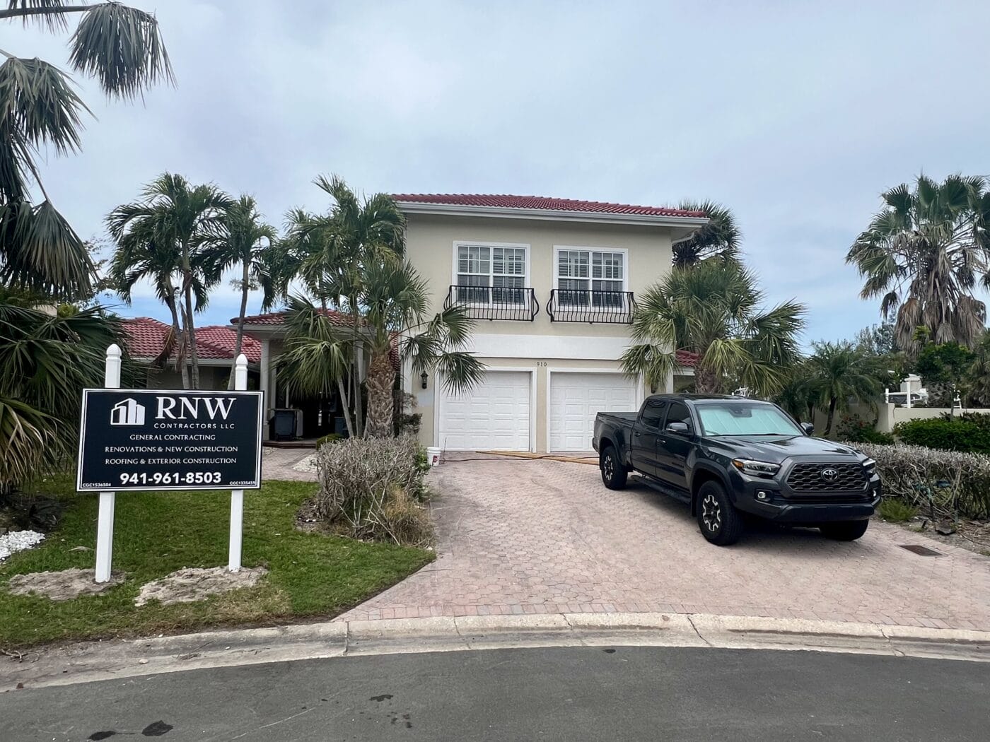 A large two-story house with a red tile roof and palm trees boasts a double garage and a black truck parked in the driveway. A contractor's sign announces an impressive whole home renovation underway, hinting at exciting transformations inside.