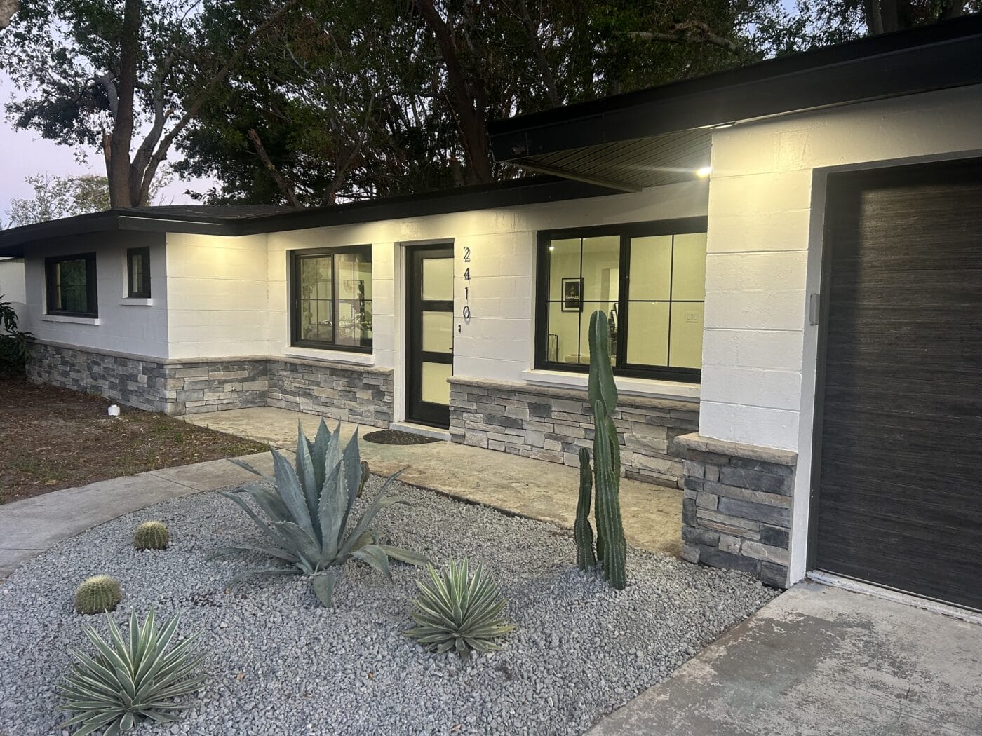 Single-story house with white walls, large windows, and a stone accent exterior. The front yard, designed by a General Contractor Sarasota FL, features gravel landscaping with cactus and agave plants.
